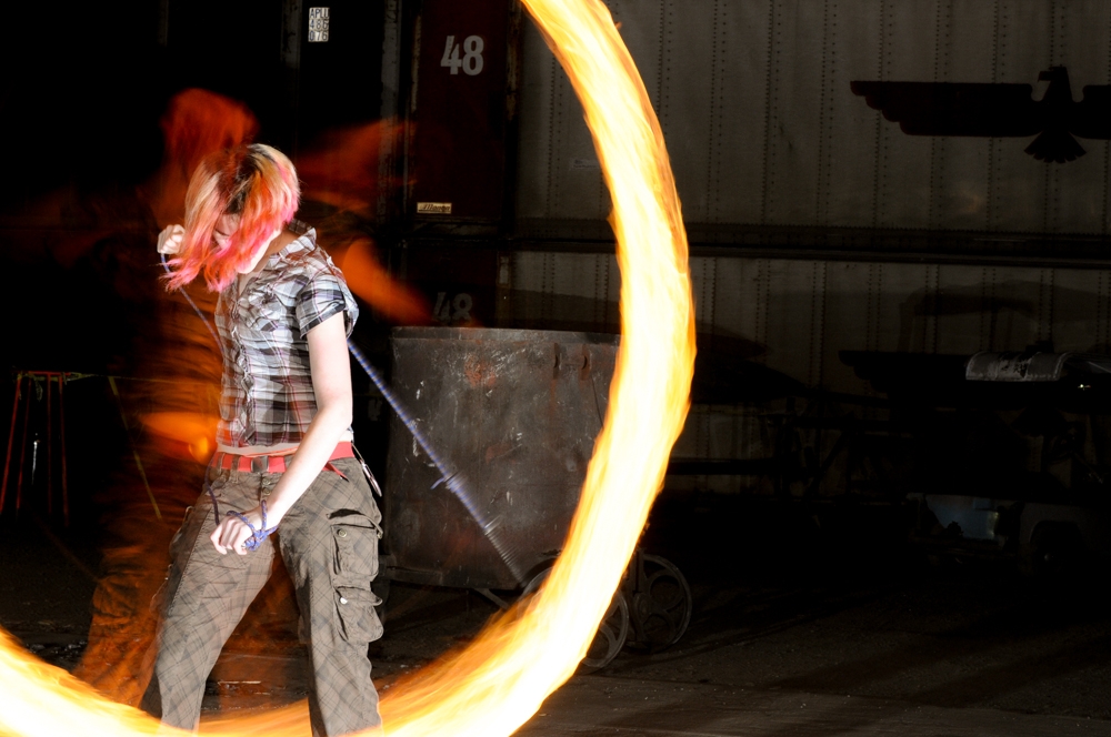 Fire Spinners photograph. Nicole spins rope dart. I used a setup with rear-synch flash and longer exposure, to that I could get the motion of the fire and also a still image of the person at the same time.  See the <a href='/technology/rear-sync-flash-photography/'>full explanation of rear-curtain flash.</a>